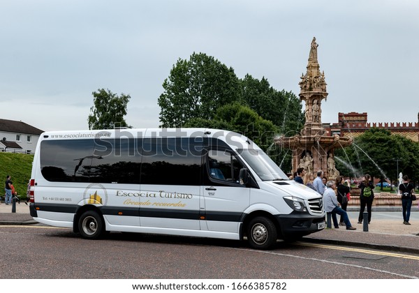 GLASGOW, SCOTLAND - JULY\
31, 2019: Mercedes-Benz Sprinter touristic shuttle bus of the\
Escocia Turismo company in the Glasgow Green park in front of the\
Doulton Fountain