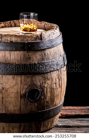 Glass of aged brandy or whiskey on the rocks and old oak barrel