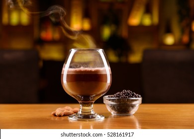 Glass with alcohol, coffee, cocoa and chocolate on a layers. Almonds and chocolate balls on a wooden table.