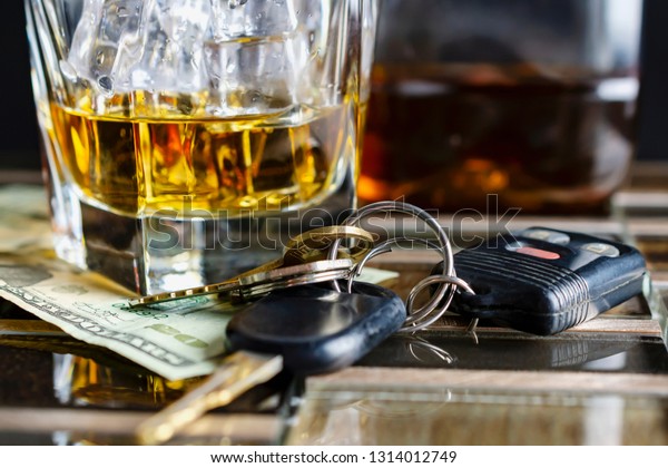 Glass of alcohol with ice, keys, and money.  Close up\
view with nearly empty bottle in background fading into black\
background.  Suggestive of drinking and driving, alcohol abuse, or\
alcoholism.  