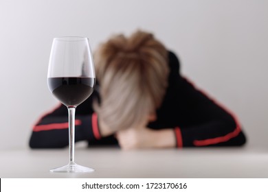 Glass with alcohol on blurred view of a lonely and desperate drunk woman