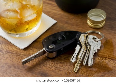 A glass of alcohol on top of a bar table along with a set of car keys.