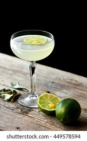 The glass of alcoholic cocktails Daiquiri consists of rum on the leaves of lime, elderflower syrup stands on wooden table on black background