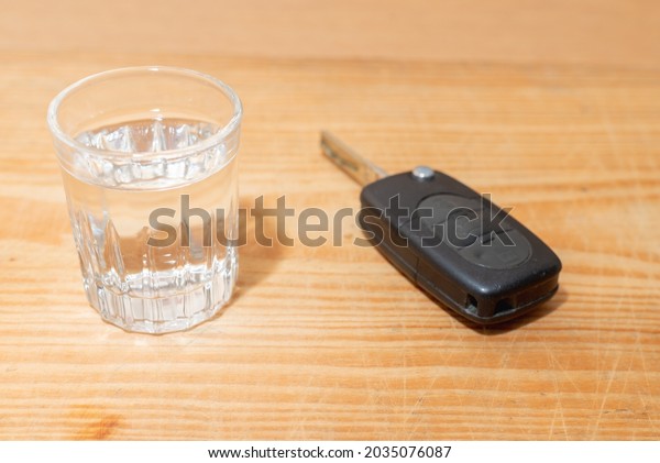 Glass of alcoholic drink and car key, on wooden\
table background.Alcoholic drink and car keys - do not drink and\
drive concept.