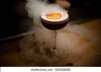 Glass Of Alcoholic Drink With Foam Decorated With Slice Of Citrus Stands On Smoky Bar Counter.