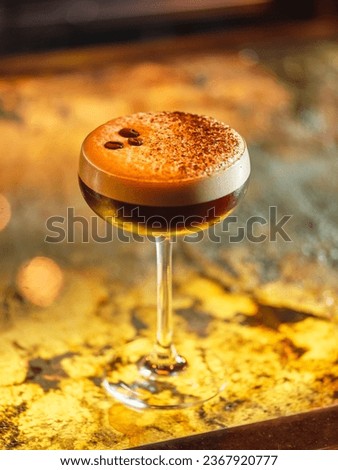 Glass with alcoholic espresso martini cocktail decorated with coffee beans and cocoa powder on white froth served on counter in bar