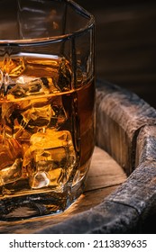 Glass of amber-colored whiskey stands on barrel of whiskey with soft focus close-up. Brandy with ice alcoholic drink with aroma of cognac. - Shutterstock ID 2113839635