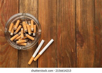 Glass ashtray with cigarette stubs on wooden table, flat lay. Space for text