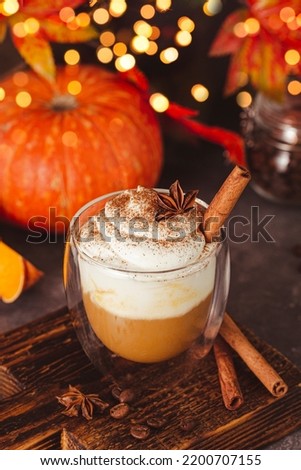 A glass of autumn pumpkin latte with whipped cream and spices. Coffee with pumpkin and cinnamon on a dark background, bokeh lights, vertical photo. High quality photo