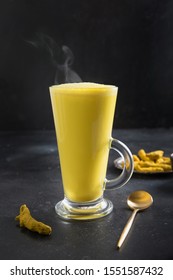 Glass of ayurvedic golden turmeric latte milk with curcuma powder, over black table. Vertical shot.