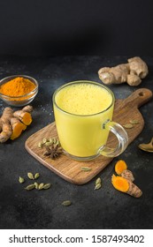 Glass Of Ayurvedic Golden Turmeric Latte Milk With Curcuma Powder Over Black Table. Vertical Shot. Masala Haldi Doodh