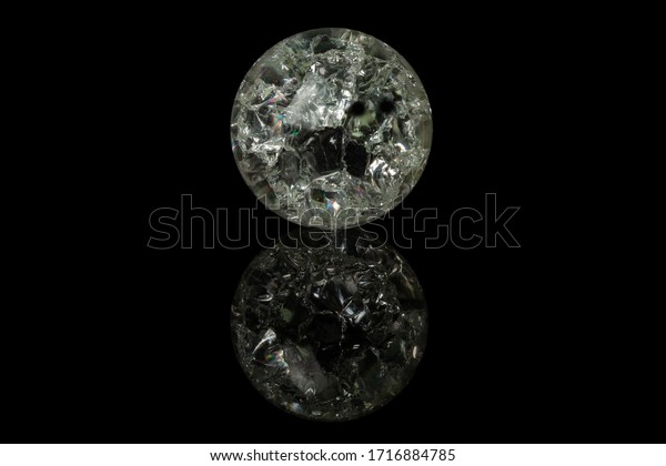 A glass ball with an\
abstract pattern lies on a glossy black glass, in which its\
reflection is visible