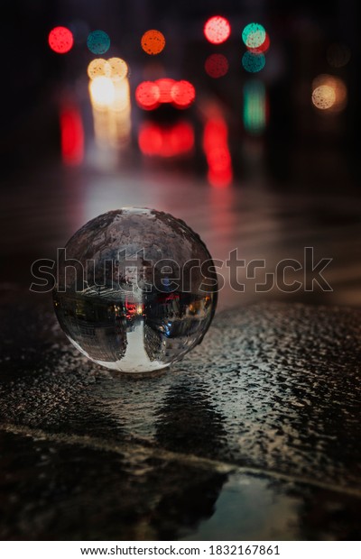 Glass ball in the street under the rain\
with some car lights out of focus on the\
background