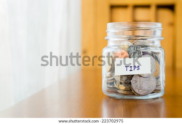Glass bank with many world coins and  tips word or\
label on saving money jar