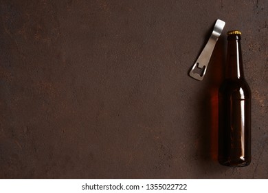 Glass beer bottle and opener on the textured brown table, copy space