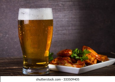 Glass of beer and chicken wings on dark wooden background