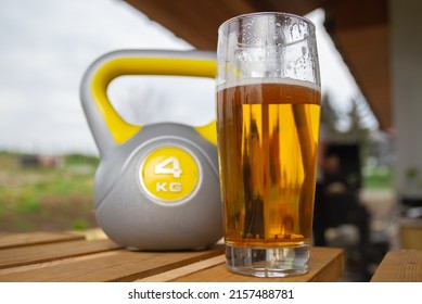 Glass Of Beer And Heavy Kettlebell Weight In Background. Contrasting Alcohol With Sports, Choice Between Healthy And Harmful Lifestyle. Cheat Day Temptation Vs Sticking To Diet.