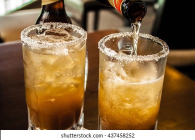 Glass of beer with mexican michelada mix and salt on the table.