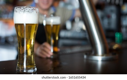 Glass Of Beer On Bar Counter Against Background Of Friendly Elderly Bartender
