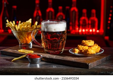 Glass Of Beer On Bar Counter. Jugs, Mugs, Pints Of Brew Beverage, Ale, Cider On Wooden Table In Pub, Bar. Backlit Dark Showcase With Craft Beer Bottles In Brewery. French Fries Fried Potatoes Snack.