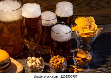 Glass Of Beer On Bar Counter. Jugs, Mugs, Pints Of Brew Beverage, Ale, Cider On Wooden Table In Pub, Bar. Backlit Dark Showcase With Craft Beer Bottles In Brewery. French Fries Fried Potatoes Snack.