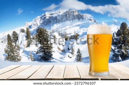 glass of beer on old wooden table against winter landscape
