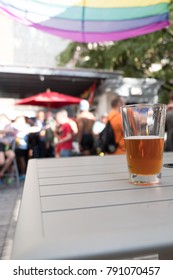 Glass Of Beer On A White Table Outside On A Rooftop Bar In NYC. Gay Men At A Gay Rooftop Bar In New York City On A Sunny Weekend Afternoon For Day Drinking On Roof Top.