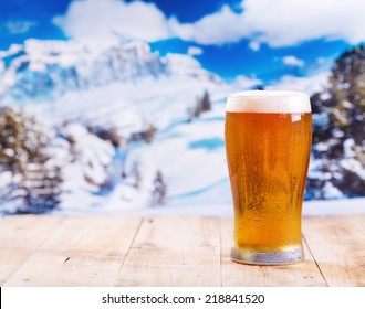 glass of beer on wooden table over winter landscape