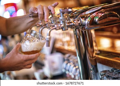 Glass Of Beer In Pub, Hand Of Bartender Pouring A Large Lager Beer In Tap, The Beer Taps In A Pub