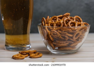 Glass of beer and salty mini pretzels in a deep glass bowl on a wooden tabletop. Popular beer snack.