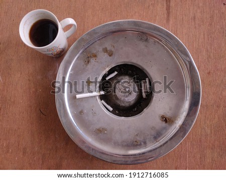A glass of black coffee and a white cigarette on an iron ashtray