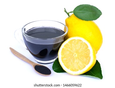 Glass of black lemonade with activated charcoal powder in wooden spoon with fresh whole and half slice yellow lemon isolated on white background.Trendy detox healthy drinks and diet concept. 