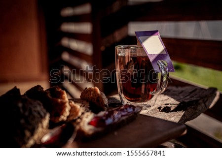 Glass of black tea in double bottom glass under the shade under sun light, winter hot drink with glass kettle of strong tea on wooden table and tea cloth, copy space