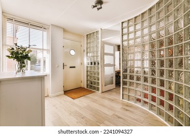 a glass block wall in a hallway with wooden flooring and white trim on the walls there is a vase full of flowers - Shutterstock ID 2241094327