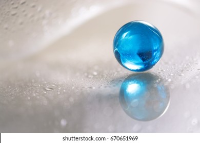 Glass blue ball on a white glass table. Abstract photo with glass and reflection. Selective focus