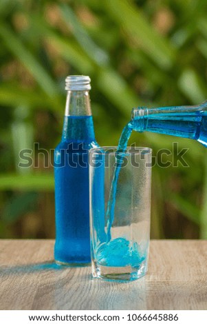 A glass with a blue drink stands on a table on a green background