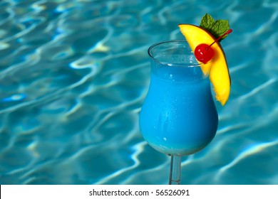 Glass Of Blue Hawaiian Cocktail On Swimming Pool Side Garnished With Mango Wedge And Maraschino Cherry