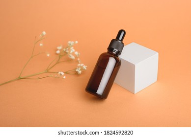 A glass bottle with aromatic oil or serum on a white cube and little twig with flower near. Natural Organic Spa Cosmetic concept. Front view.