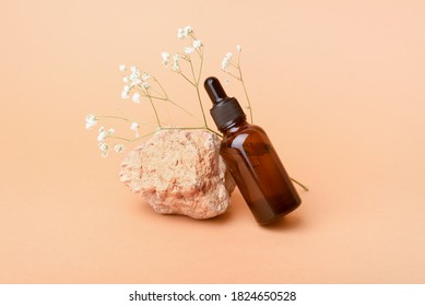 A glass bottle with aromatic oil or serum on a stone and little twig with flower near. Natural Organic Spa Cosmetic concept. Front view.