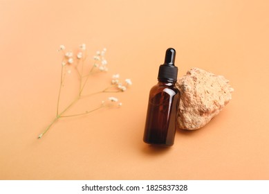 A glass bottle with aromatic oil or serum on a stone and little twig with flowers near. Natural Organic Spa Cosmetic concept. Front view.