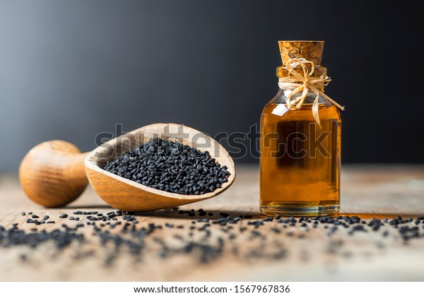 glass bottle of black cumin seeds essential\
oil , Nigella Sativa in spoon on wooden background. Organic herbal\
medicine for many diseases, black\
cumin