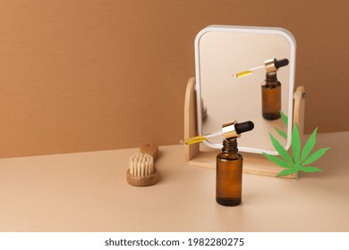 Glass Bottle Of CBD Oil, THC Tincture,mirror And Face Massage Brush Over Brown Background. Cosmetics CBD Oil. Droplet Bottle Of Cannabis Oil Extract.