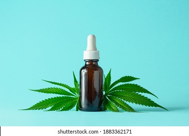 Glass Bottle of CBD or THC Oil with Hemp or Medical Cannabis Plant Leaves Isolated on Aqua Blue Green Background