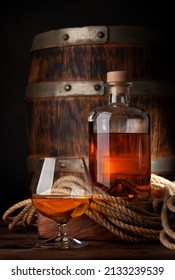 Glass And Bottle With Cognac, Whiskey Or Golden Rum. In Front Of Old Wooden Barrel