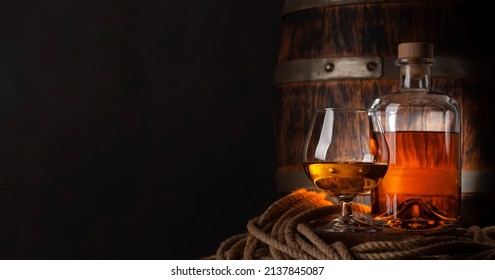 Glass And Bottle With Cognac, Whiskey Or Golden Rum. In Front Of Old Wooden Barrel With Copy Space