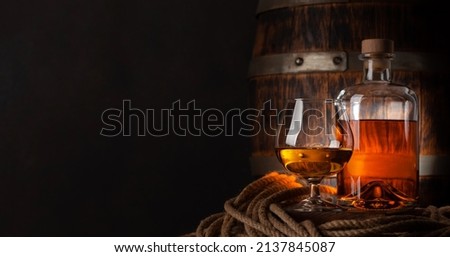Glass and bottle with cognac, whiskey or golden rum. In front of old wooden barrel with copy space