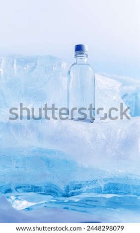 A glass bottle with cold natural drinking water stands on an ice podium against a background of transparent blocks of ice. Advertising and branding of drinking fresh water