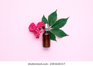 A glass bottle with dropper. Aromatic oil or face serum on pink paper background and little twig with roses flowers near. Natural Organic Spa Cosmetic concept. Flat lay. Copy space for text. Top view.