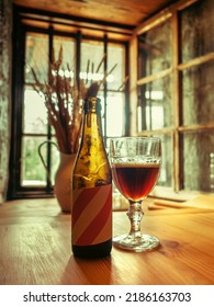 Glass Bottle And Glass Filled With Dark Beer On A Wooden Table In A Medieval Castle