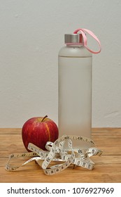 A Glass Bottle Filled With Ice Cold Water, A Measuring Tape And An Apple